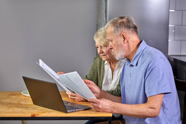 worried senior couple checking finances at home using laptop - Foto, afbeelding