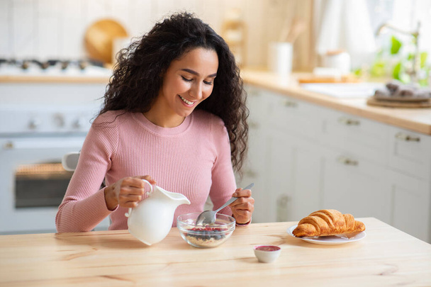 Portret van gelukkige jonge vrouw ontbijten in de keuken, eten Muesli - Foto, afbeelding