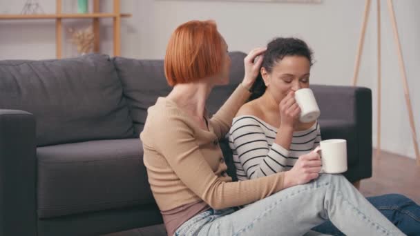 κοκκινομάλλα γυναίκα αγγίζοντας τα μαλλιά της ισπανικής φίλη πίνοντας καφέ - Πλάνα, βίντεο