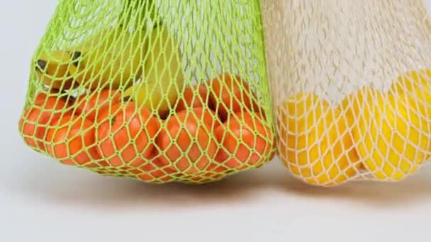 mão feminina coloca um saco de corda têxtil reutilizável com limões amarelos maduros e laranjas em uma superfície branca, recusa de plástico - Filmagem, Vídeo