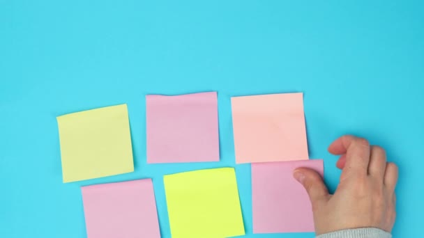 vrouwelijke hand lijmen veelkleurig papier vierkante stickers op een blauw oppervlak, multitasking - Video