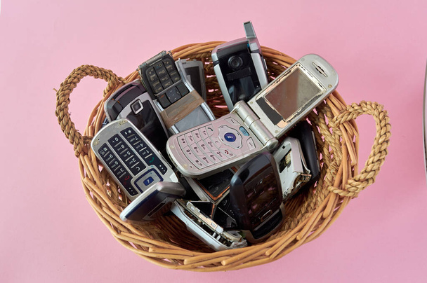 cesta de vime, com telefones celulares quebrados, tecnologia de reciclagem, início dos anos 2000 em fundo rosa e espaço de cópia,. - Foto, Imagem