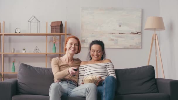 лесбиянка держит пульт дистанционного управления рядом с латиноамериканской подругой с попкорном   - Кадры, видео