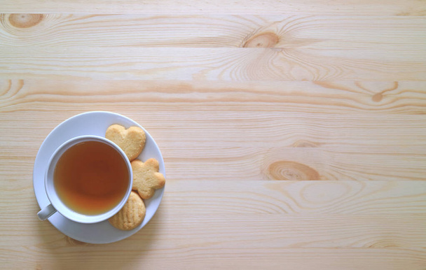 木のテーブルの上でバタークッキー3つでお茶のカップのトップビュー - 写真・画像