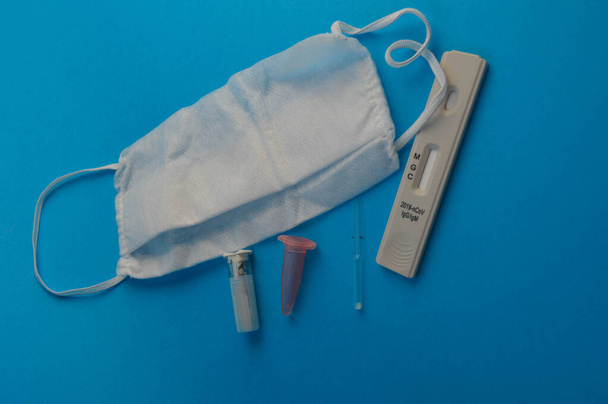 Antikörpertest. neben dem Test eine Einmalmaske, eine Lanzette und eine Pipette für die Analyse mit einem Gefäß für Blut. Blutanalyse. Selbstdiagnose für Coronavirus. - Foto, Bild