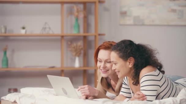 alegre interracial novias viendo comedia película en portátil en dormitorio - Imágenes, Vídeo