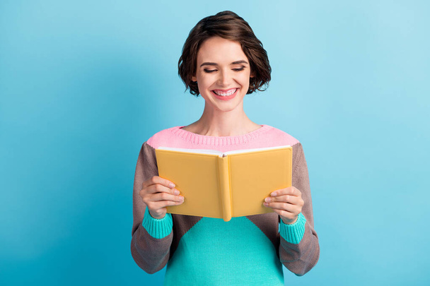 Photo portrait of happy smiling girl holding yellow book in two hands isolated on pastel light blue colored background - Фото, зображення