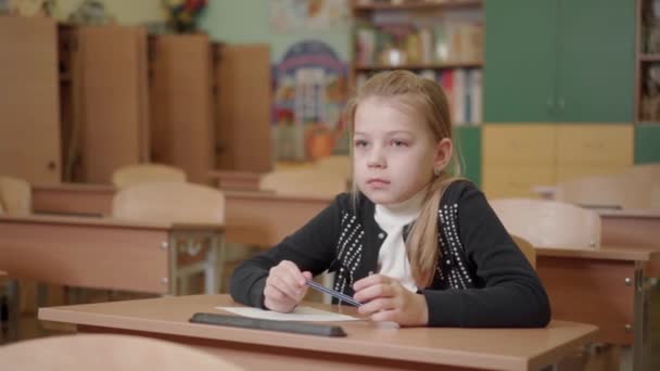 Portret van een schoolmeisje dat aan een bureau zit en een pen in haar handen houdt. - Video