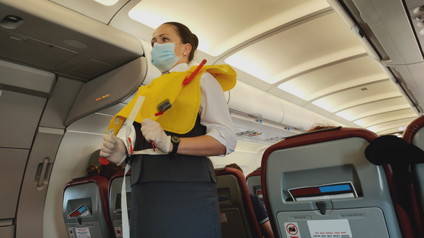 Woman stewardess flight attendant in face mask presenting life vest on board before the flight departure - Photo, Image
