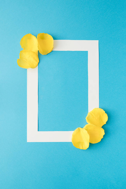 Svislý bílý rám se žlutými okvětními lístky růží na modrém pozadí.Minimální koncept lásky. - Fotografie, Obrázek