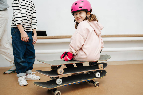 Charming girl in pink helmet sitting on a triple skate stack at indoor skatepark - Фото, изображение