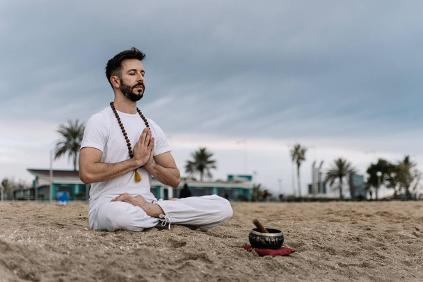 Bonito caucasiano com barba praticando exercícios de meditação na praia ao amanhecer - Foto, Imagem