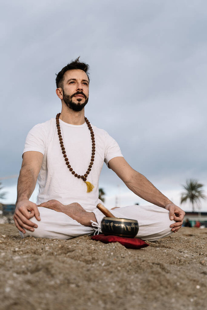 Кавказский мужчина с бородой практикует медитационные упражнения на пляже на рассвете - Фото, изображение