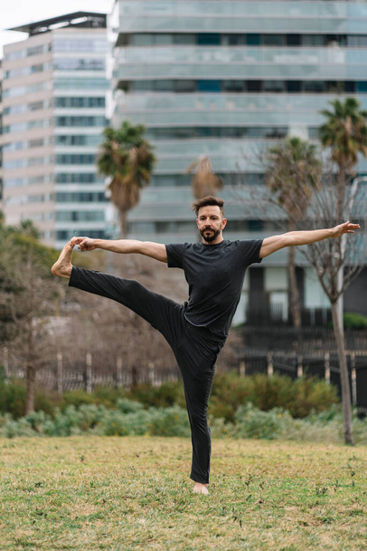 Healthy man in darkclothes practising yoga exercises in a city park - Foto, Imagen