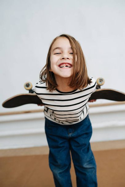 Toothless little girl posing with skateboard, playing cute, leaning forward - Photo, image