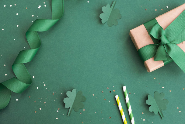 Сочинение дня Святого Патрика. Подарочная коробка, клевер и праздничный декор на зеленом фоне. Вид сверху, плоский, копировальное пространство - Фото, изображение