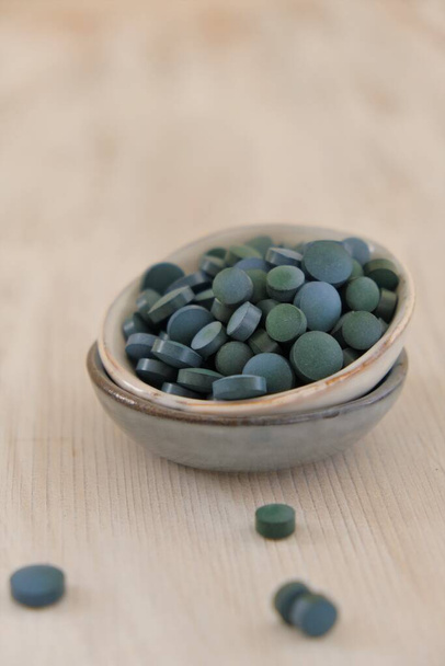 Spirulina algae green in tablets in ceramic cups on a light wooden shabby background..Dietary supplements.Super food. Healthy organic seaweed.Healthy lifestyle. Food product.Dry algae tablets - Fotó, kép