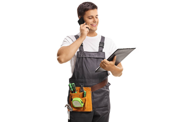 Repairman in a uniform holding a clipboard and talking on a mobile phone isolated on white background - Φωτογραφία, εικόνα