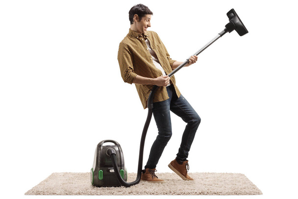 Cheerful young man playing a guitar with a vacuum cleaner isolated on white background - Φωτογραφία, εικόνα