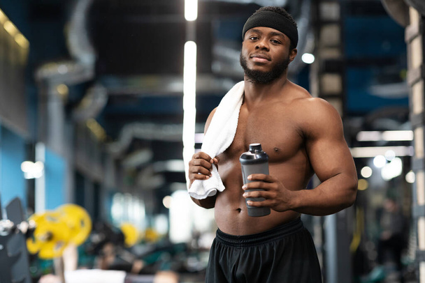 Shirtless black bodybuilder with water and towel at gym - Fotó, kép