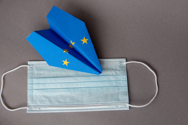 medical face mask antiseptic and paper plane in EU european union flag - concept traveling abroad during coronavirus pandemic, new flight ban rules travel, aviation business - Photo, Image