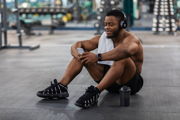 Relaxed sportsman listening to music on mobile phone, gym interior - Photo, image