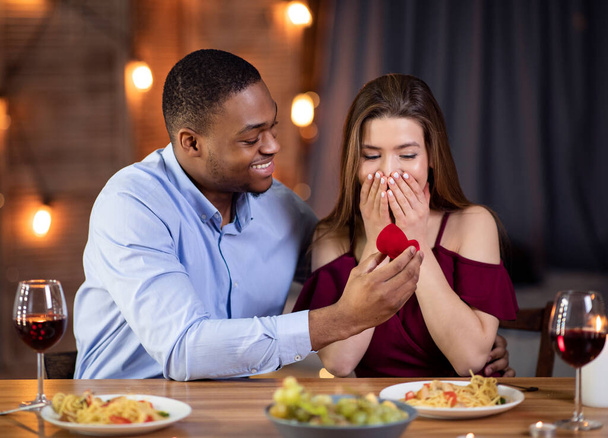 Knappe Afrikaanse man die zijn blanke vriendin ten huwelijk vraagt in restaurant - Foto, afbeelding