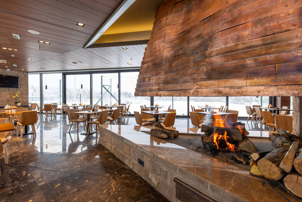 Interior of an empty mountain restaurant with large fireplace in the middle - Фото, изображение