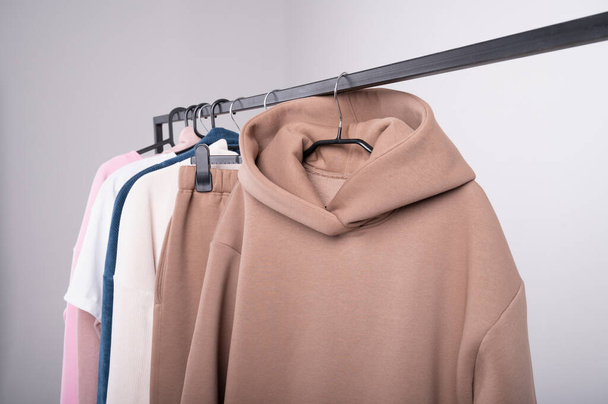 Women's minimal fashion pastel clothes. Stylish female t-shirts, hoodie, pants on hanger on white background. Spring cleaning home wardrobe. High quality photo - Photo, Image
