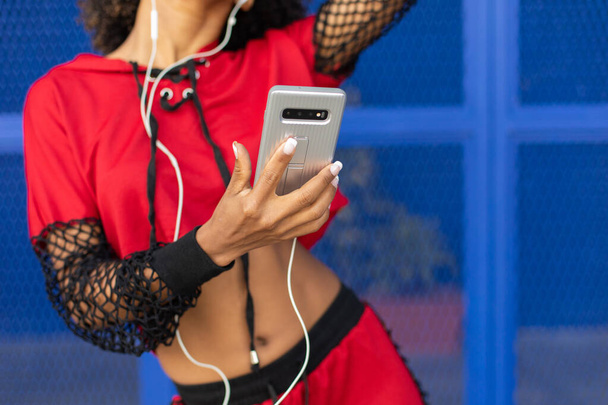 Black urban stylish female dancer using smartphone for listening music outside. - Zdjęcie, obraz