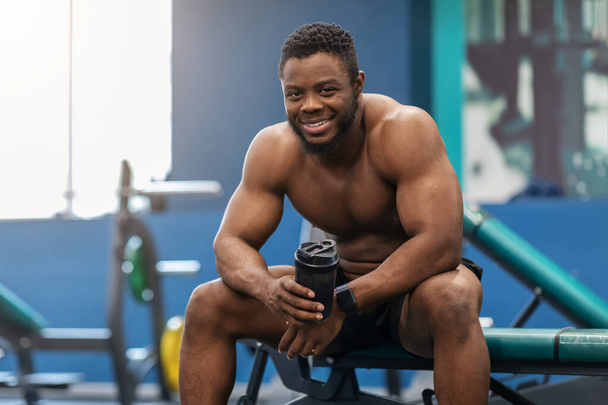 Χαμογελώντας αφροαμερικάνικη shirtless bodybuilder πίνοντας πρωτεΐνη - Φωτογραφία, εικόνα