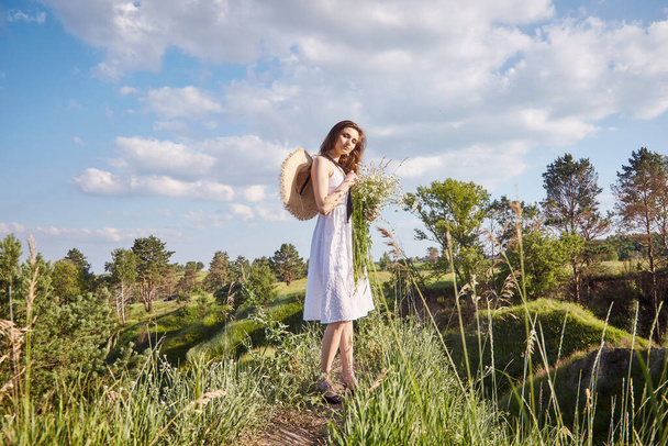 a girl in a white dress with a bouquet of flowers is walking in the field - Foto, Imagen