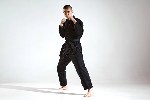 Sportive guy trainer in black kimono fighter posing in karate stance on studio background with copy space - Фото, зображення