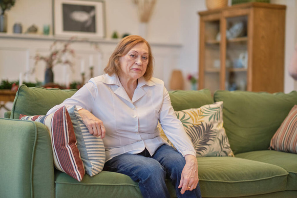 Portrait d'une femme âgée assise sur un canapé à la maison de retraite. Femme blanche assise sur un canapé et regardant la caméra. Soins aux retraités solitaires. - Photo, image