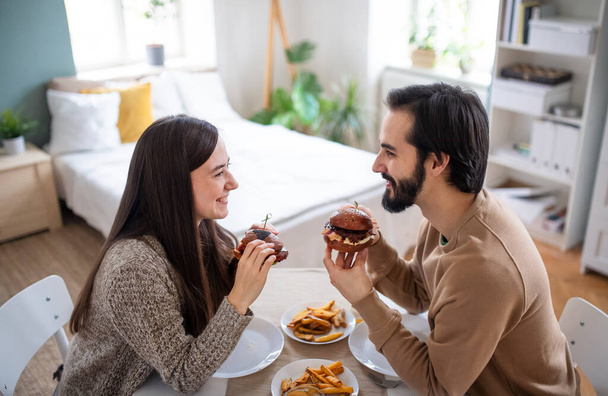 Young couple in love eating hamburgers indoors at home. - Photo, image