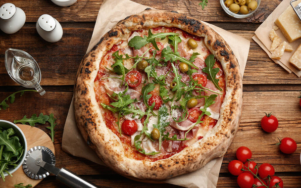 Tasty pizza with meat and arugula on wooden table, flat lay - Fotografie, Obrázek