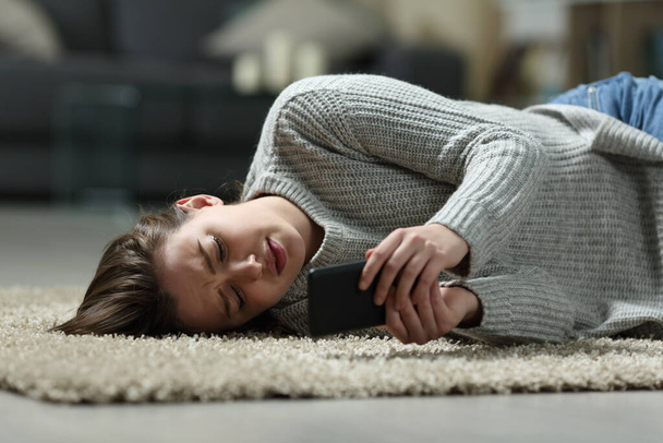 Sad teen reading bad news on smart phone lying on the floor at home - Фото, зображення