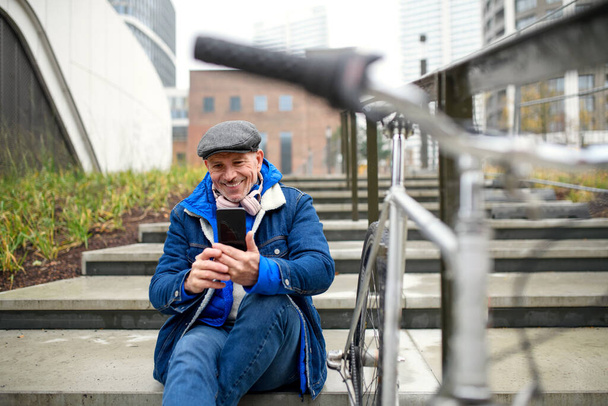 Happy senior man with bicycle outdoors in city, taking selfie. - Foto, afbeelding