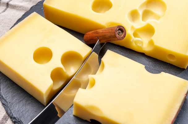 Blok švýcarské střední tvrdý žlutý sýr emmental nebo emmentaler s kulatými otvory a nůž na sýr zblízka - Fotografie, Obrázek