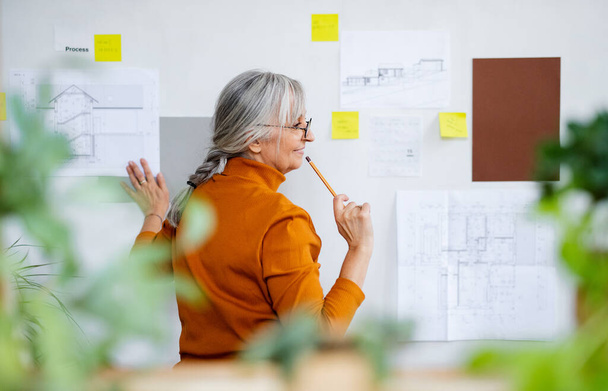 Rear view of senior woman architect standing indoors at home, working. - Foto, Imagen