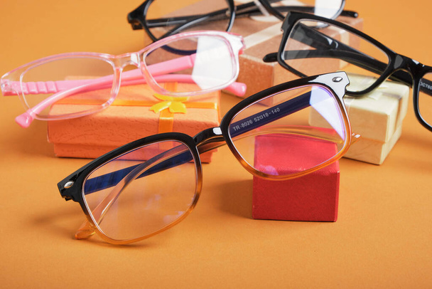 glasses on a small rted gift box, small gift boxes and different frames for glasses on a brown background copy space, - Φωτογραφία, εικόνα