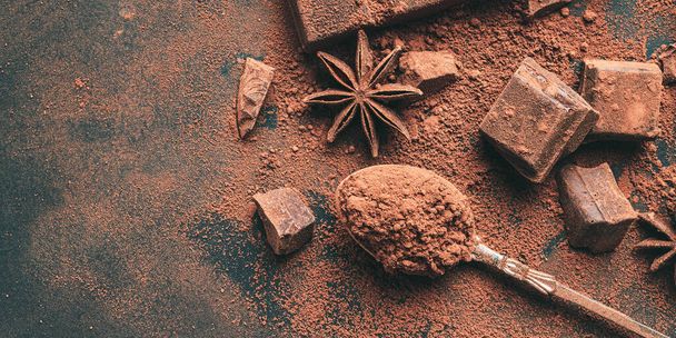 Cacao marrone in polvere nel cucchiaio e cubetti di cioccolato tritati vista dall'alto su sfondo scuro con spazio di copia. - Foto, immagini