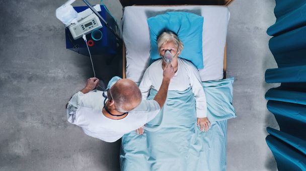 Άποψη του γιατρού και covid-19 ασθενή με μάσκα οξυγόνου στο κρεβάτι στο νοσοκομείο, έννοια coronavirus. - Φωτογραφία, εικόνα