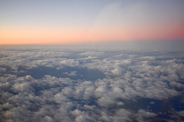  Όμορφο πορτοκαλί χρώμα του ορίζοντα σε μπλε ουρανό με λευκά σύννεφα που επιπλέουν στον ουρανό ηλιοβασίλεμα. Προβολή από το παράθυρο του αεροπλάνου. - Φωτογραφία, εικόνα