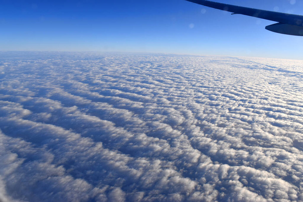 Landschaft aus weißen Wolken, die über blauem Himmel schweben. aus großer Höhe betrachtet. Aus dem Flugzeugfenster gesehen. - Foto, Bild