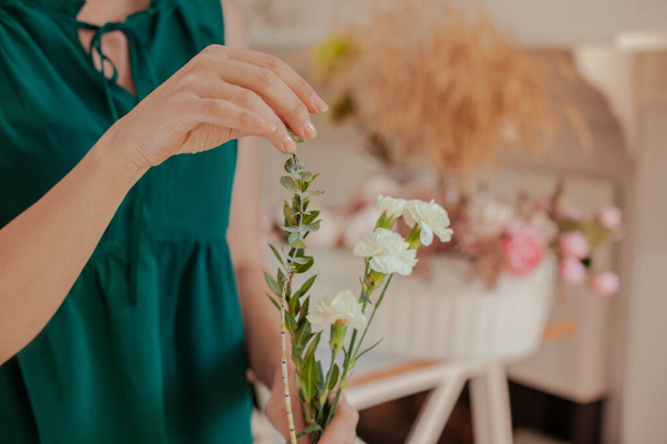 Close up of young woman arranging floral bouquet with white carnations, eucalyptus leaves and green chrysanthemum. Florist couse. How to cut stems and arrange flowers. - Foto, imagen
