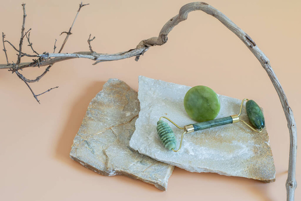 Gua sha roller for face massage on the natural stones podium with dry brunch element, neutral beige background. Health care, wellness concepts. Mockup photo with space for your text or logo.  - Photo, Image