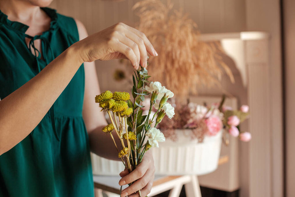Close up of young woman arranging floral bouquet with white carnations, eucalyptus leaves and green chrysanthemum. Florist couse. How to cut stems and arrange flowers. - Photo, image