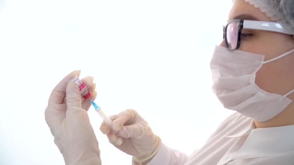 Młoda, kaukaska lekarka trzyma strzykawkę i butelkę szczepionki przeciw koronawirusowi. Koncepcja leczenia zakażenia koronawirusem, szczepienie COVID-19 - Materiał filmowy, wideo