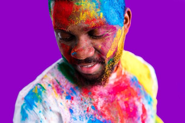 Afro american man celebrate holi festival in violet studio background - Zdjęcie, obraz
